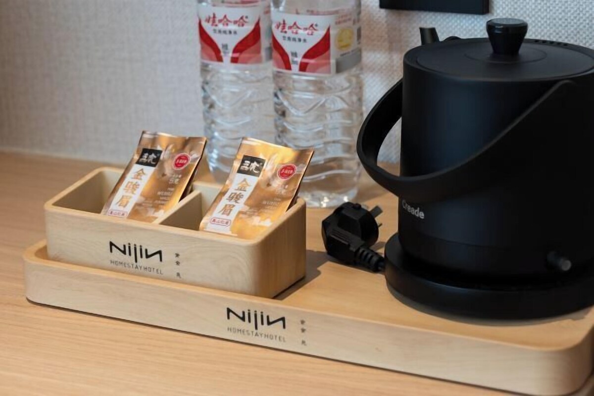 A wooden tray with three packaged items and a black electric kettle on a table.