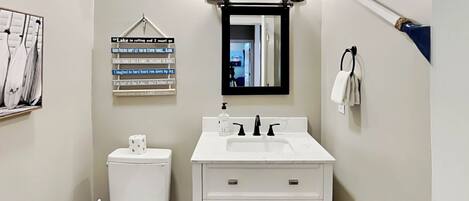 A bathroom with a white toilet, a sink with a mirror above it, and a towel rack. There is a sign on the wall with various phrases.