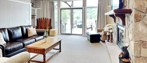 A spacious living room with a black leather sofa, a wooden coffee table, and a stone fireplace.