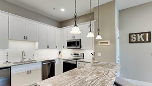 Una cocina moderna con armarios blancos, encimera de mármol e iluminación colgante.