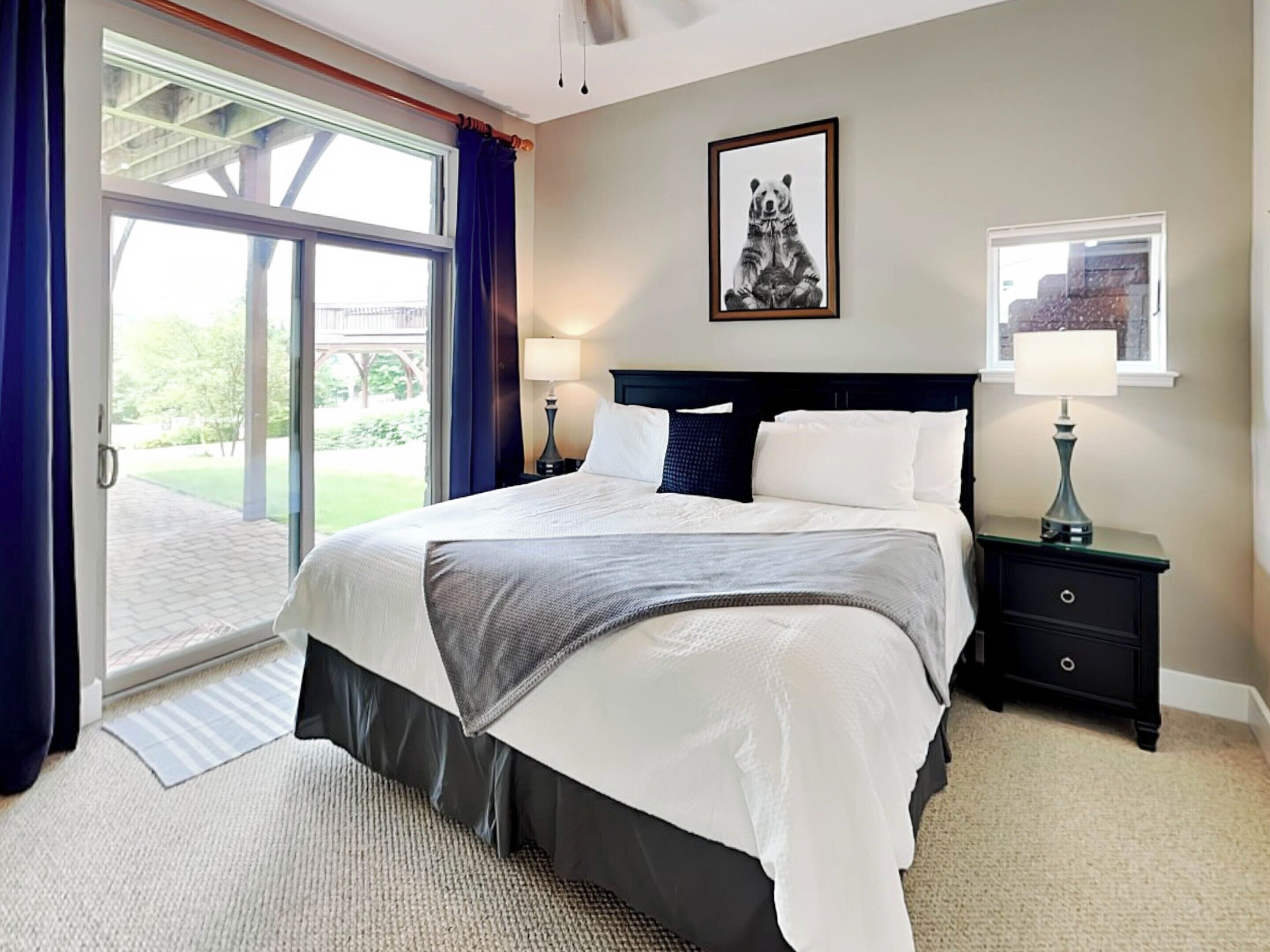 A bedroom with a large bed, two bedside tables, a window with a view, and a framed picture on the wall.