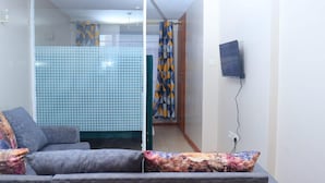 A living room with a grey sofa, a TV mounted on the wall, and a bathroom with a tiled shower area. - Impeccable 1-bed Apartment in Nairobi (Nairobi)