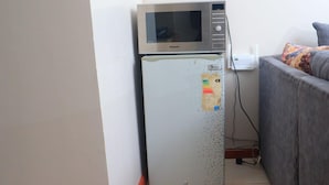 A compact refrigerator with a microwave on top, situated in a corner of a room with a grey sofa and a small table with a power strip. - Impeccable 1-bed Apartment in Nairobi (Nairobi)