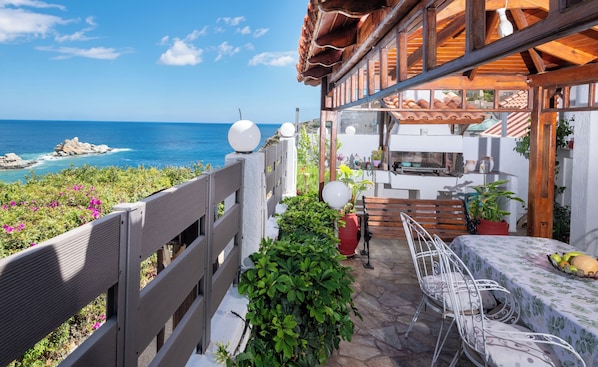 A terrace with a view of the sea, a wooden pergola, a grill, and outdoor seating.