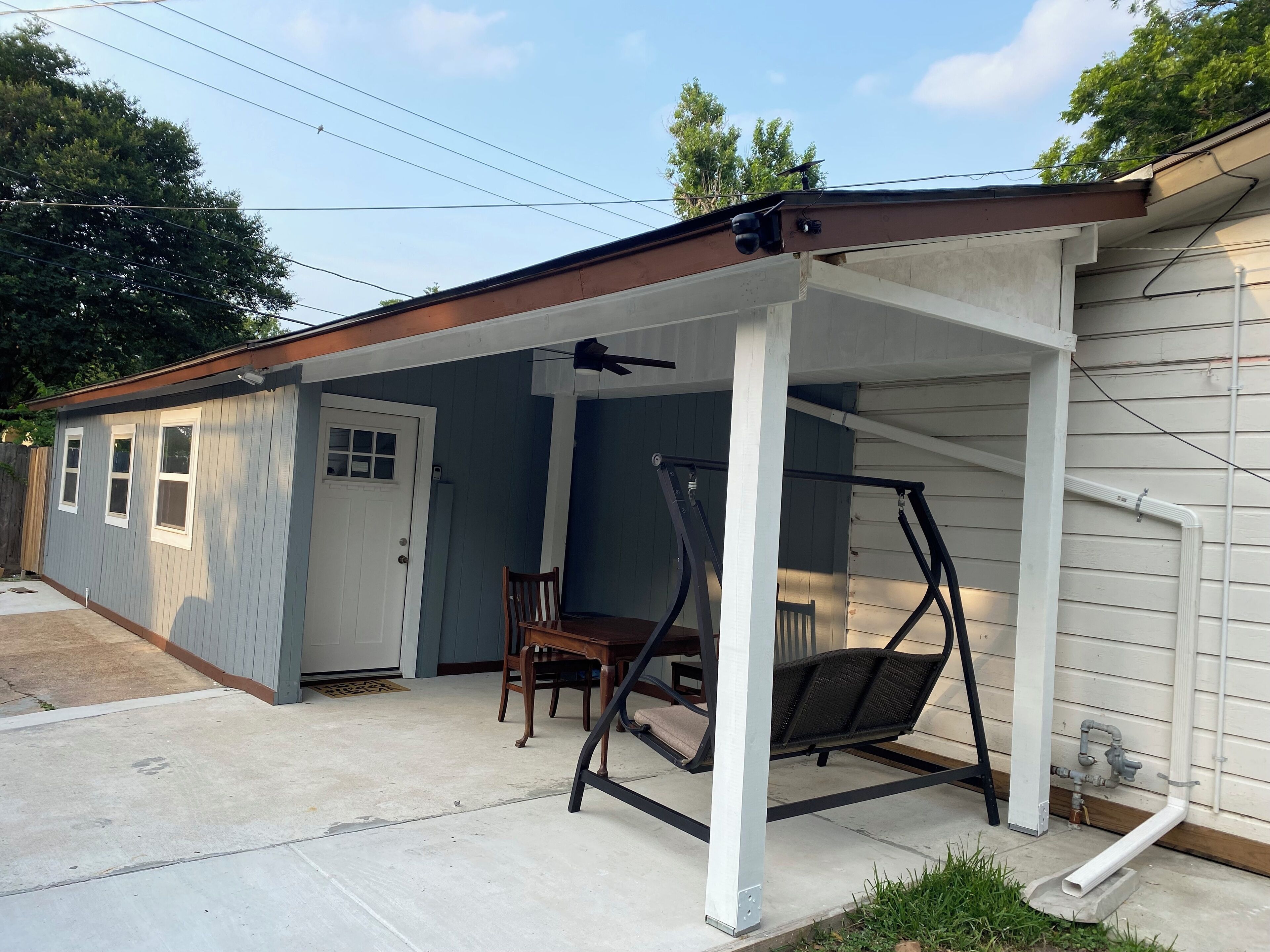 Un'area patio coperta con altalene, un tavolo da pranzo con sedie e una porta che dà su un garage.
