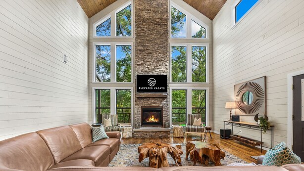 A spacious living room with a stone fireplace, leather sofas, and large windows. - Your Family-Fun HQ w/Hot Tub, Firepit, 2 Gamerooms (Broken Bow)