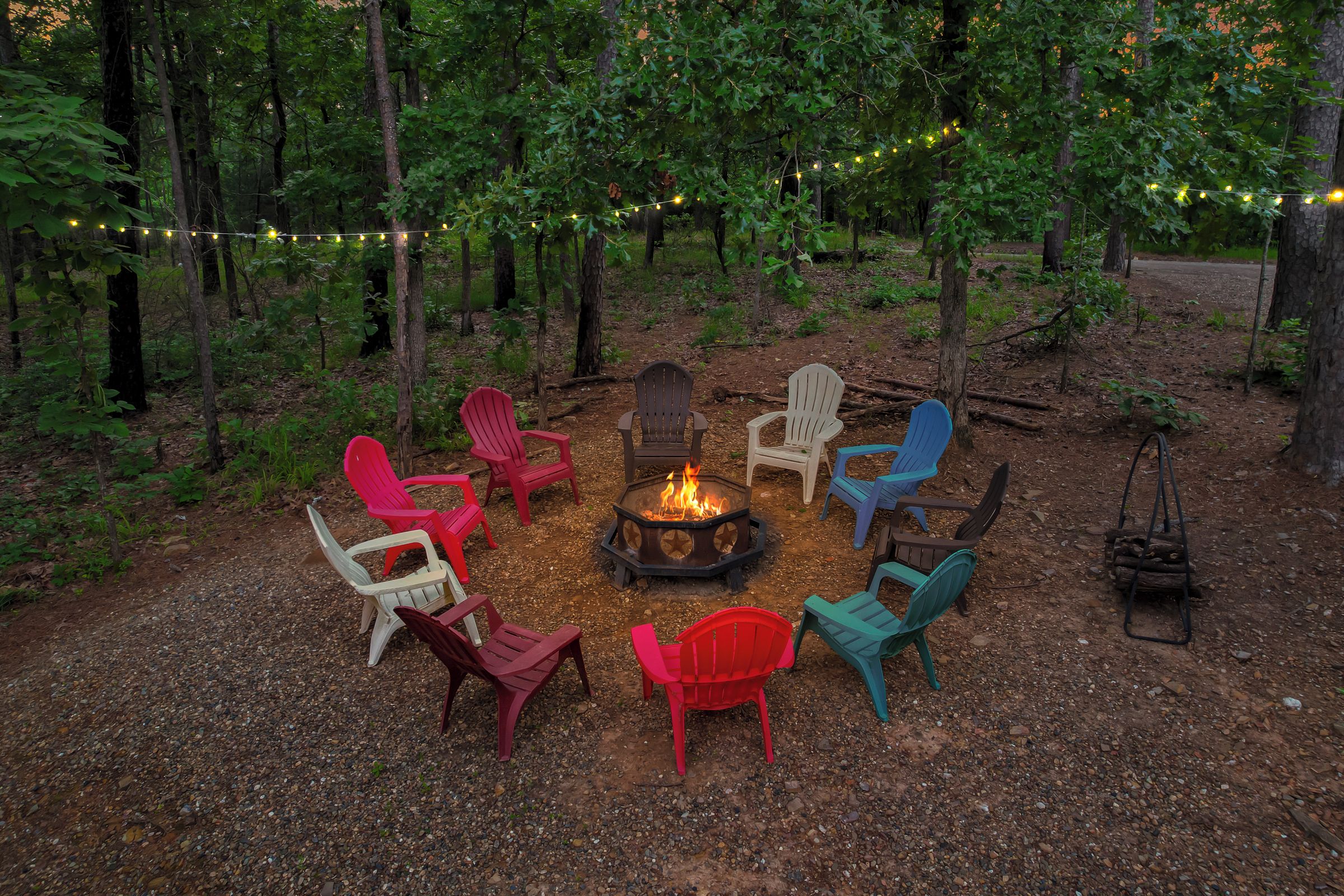 A fire pit surrounded by colorful Adirondack chairs in a forest setting.