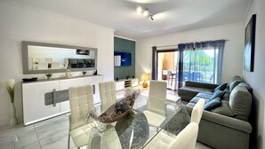 A modern living room with a glass dining table, a sofa, and a TV. - VILAMOURA PRESTIGE 2 WITH POOL by HOMING (Vilamoura)