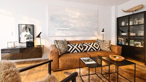 Ein modernes Wohnzimmer mit einem braunen Ledersofa, gemusterten Kissen, einem Couchtisch, einem Bücherregal und einem großen abstrakten Gemälde an der Wand.