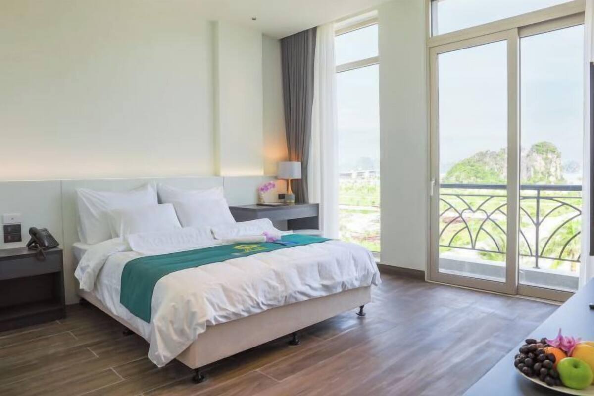 A hotel room with a bed, a nightstand, a lamp, and a view of greenery outside.