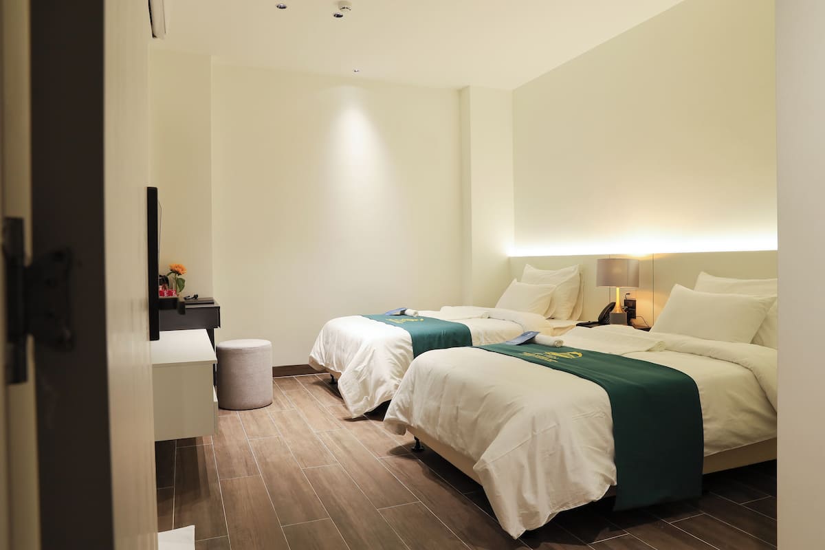 A hotel room with two beds, a bedside table, a lamp, and a mirror.