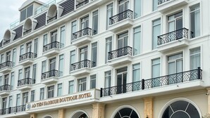 A multi-story boutique hotel with a classic architectural style, featuring arched windows and balconies with wrought iron railings. - Ao Tien Harbour Boutique Hotel (Van Don)