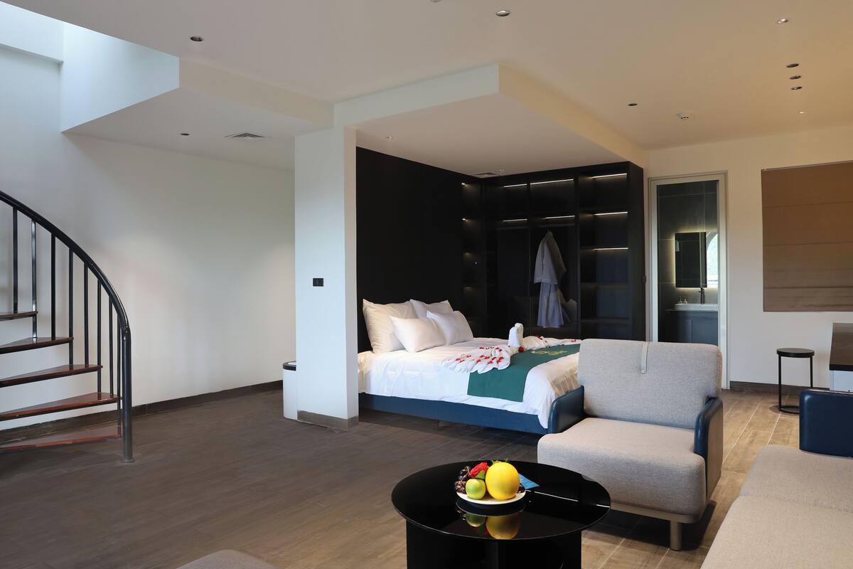 A modern hotel room with a bed, a seating area, and a staircase.