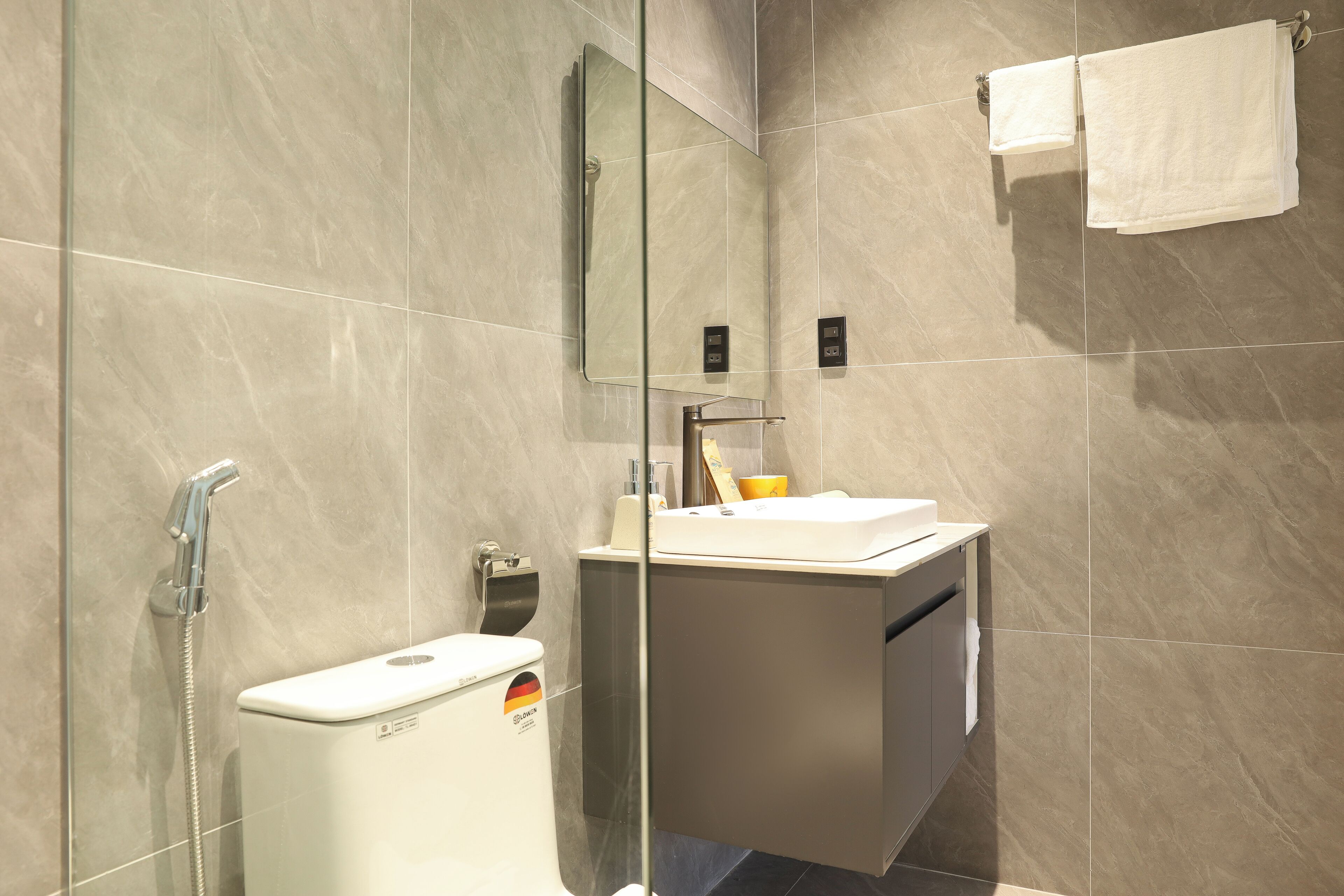 A modern bathroom with a glass-enclosed shower, a toilet, and a sink with a mirror above.