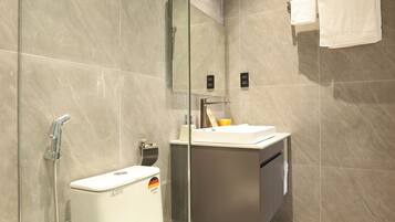 A modern bathroom with a glass-enclosed shower, a toilet, and a sink with a mirror above.