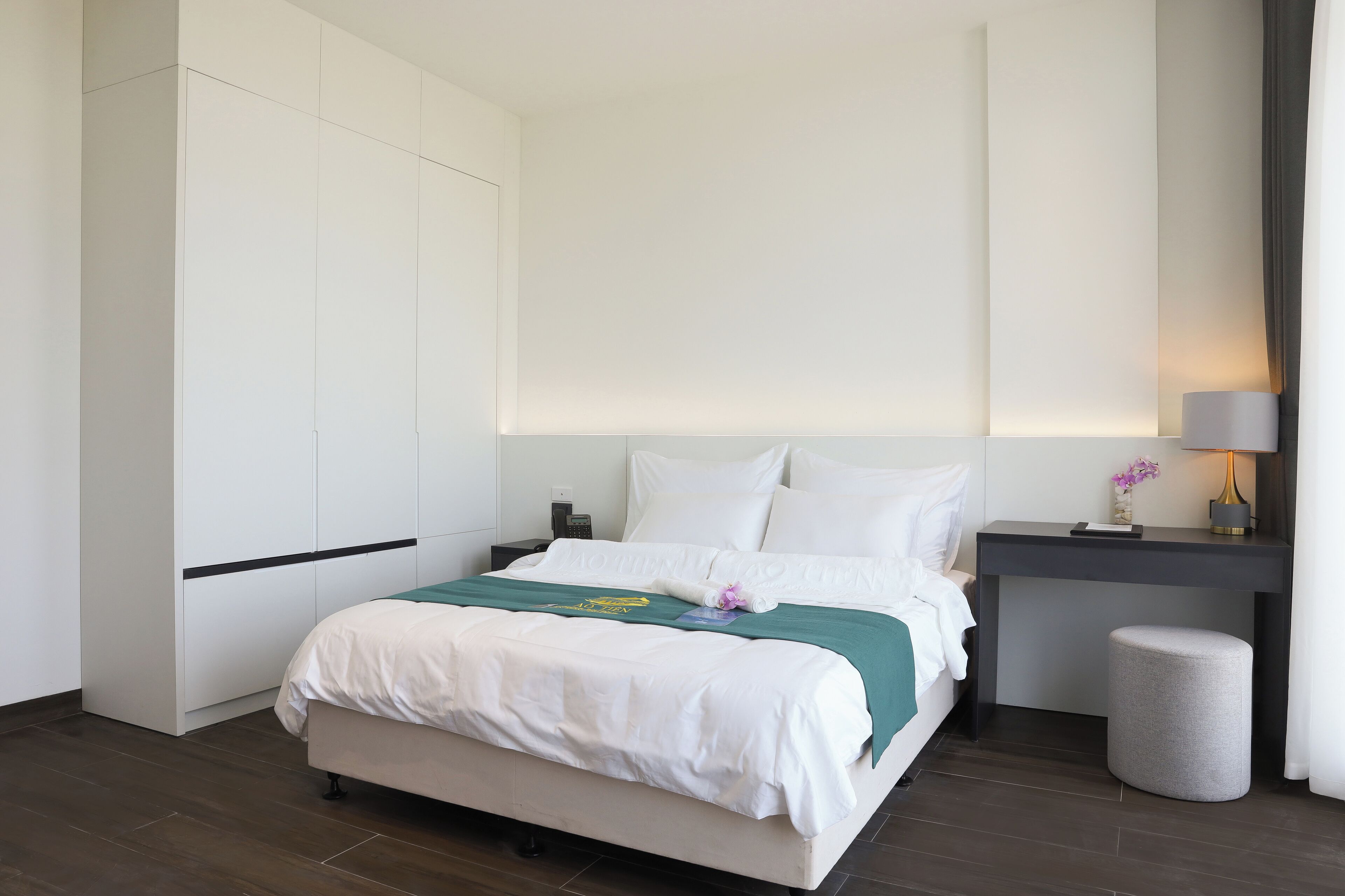 A hotel room with a bed, bedside tables, a desk, and a lamp.