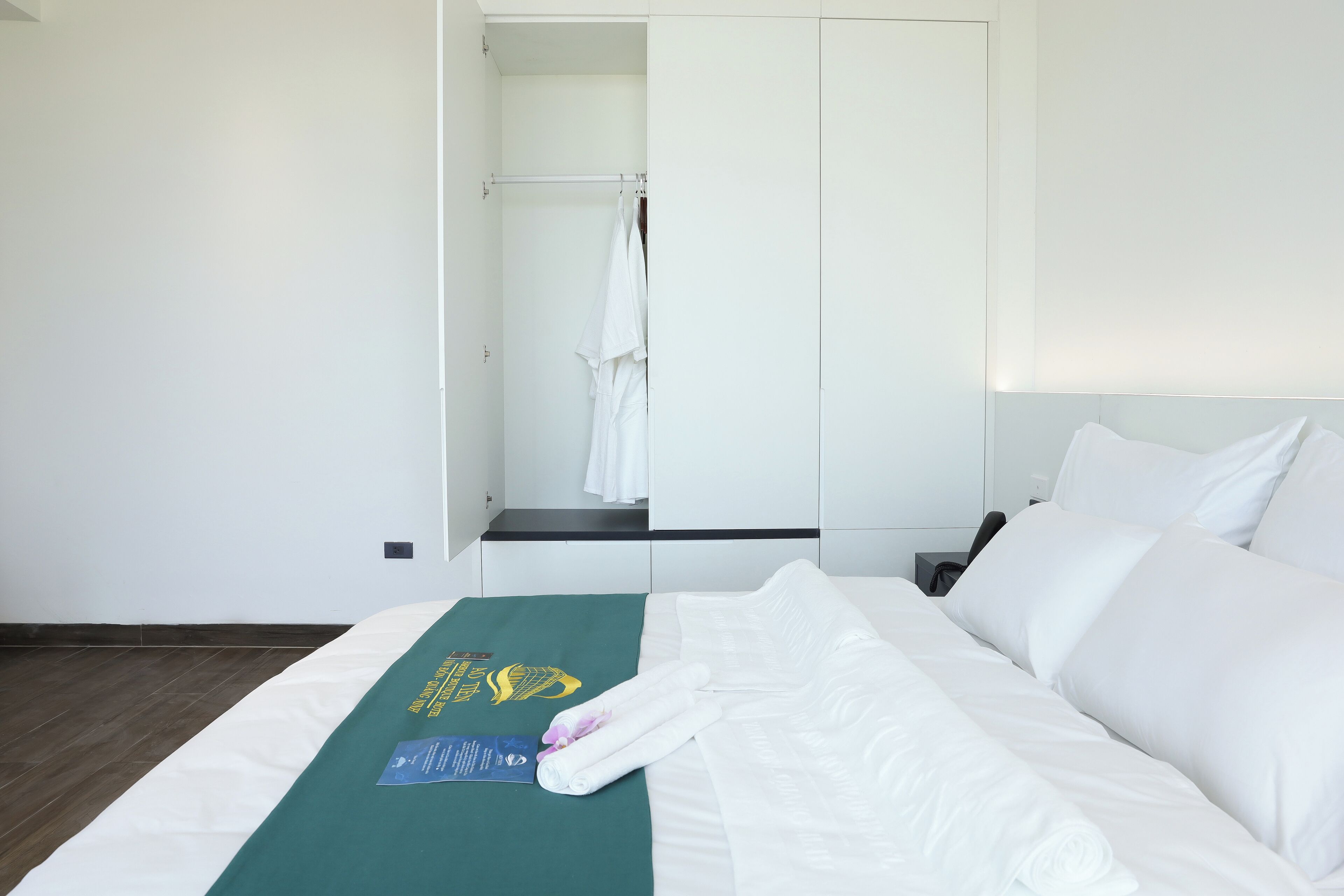 Habitació d'hotel amb un llit ben fet, una tovallola verda i una tovallola doblegada damunt del llit.