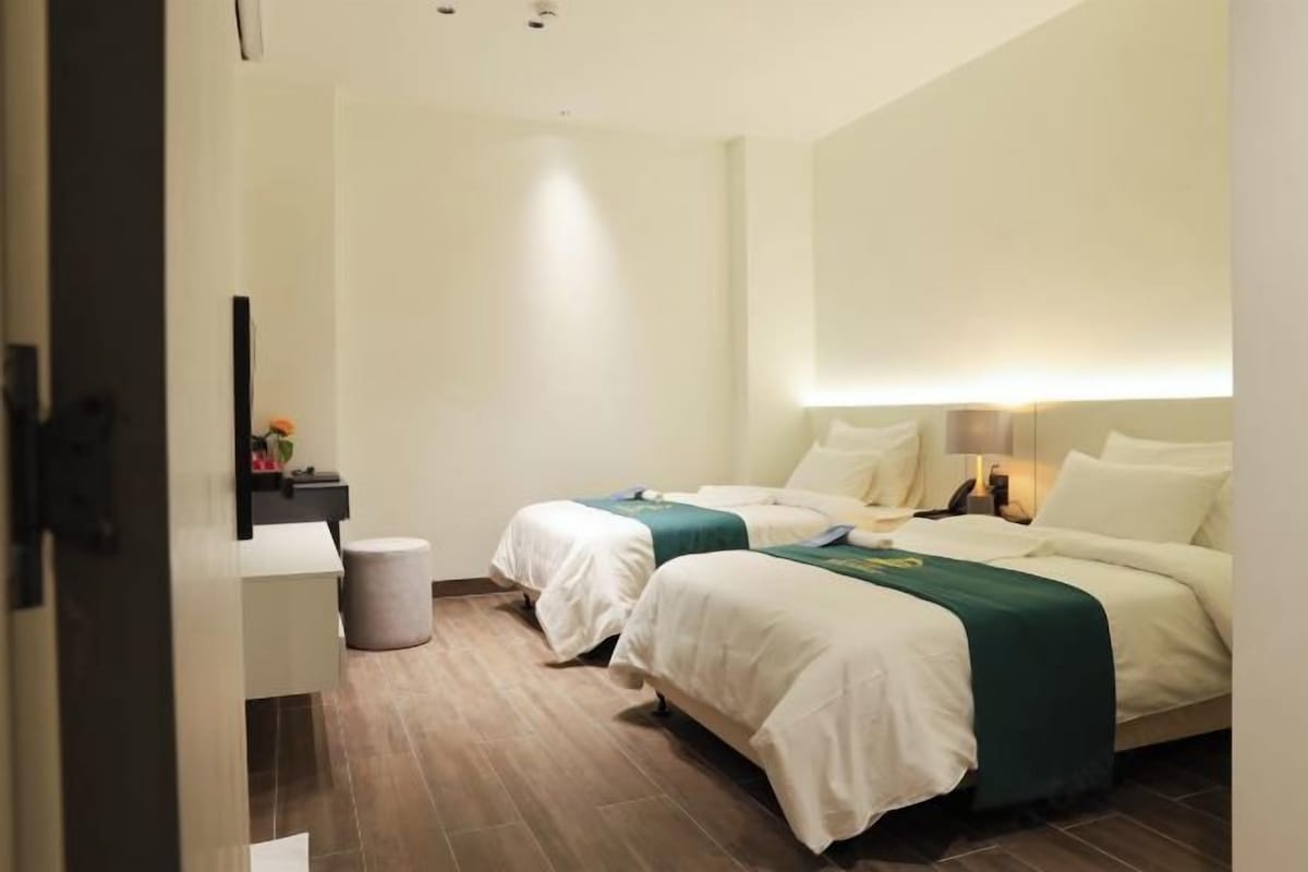 Habitación de hotel con dos camas, una mesita de noche pequeña, una silla y un espejo grande.