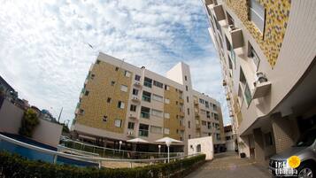 Un edificio de varios pisos con fachada decorativa, un espacio exterior cubierto con asientos y un área de estacionamiento con un automóvil.
