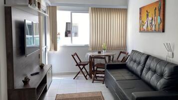 Una sala de estar moderna con un televisor de pantalla plana, un sofá de cuero, una mesa de comedor con sillas y un ventilador de techo.