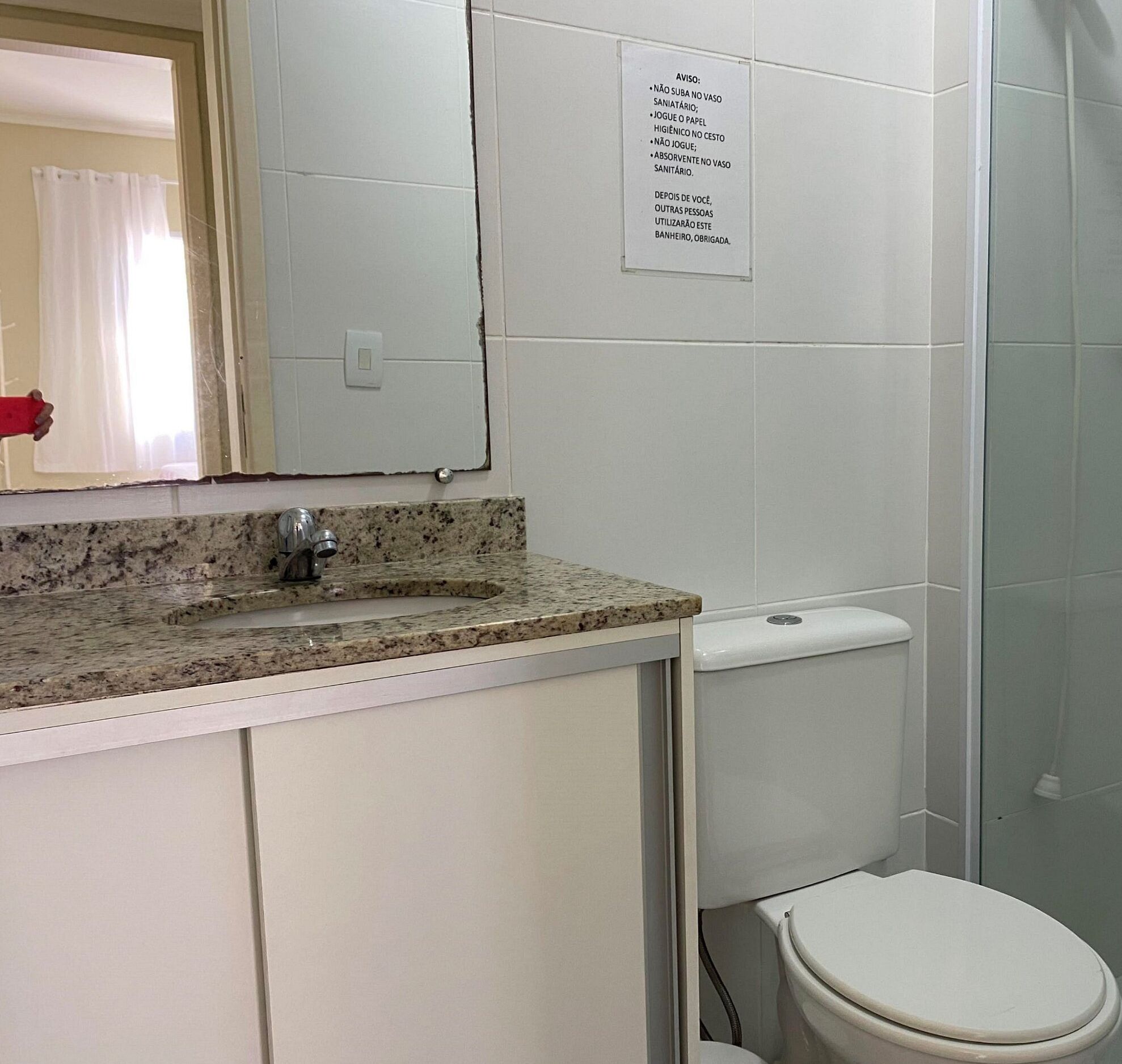 A bathroom with a sink, mirror, toilet, and a sign with hygiene instructions.