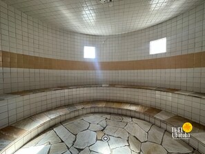 A circular room with tiled walls and a stone floor, featuring two small windows and a central drain. - Thel Ubatuba - Apto 116/D, Costa Atlântica - Pé na Areia (Ubatuba)