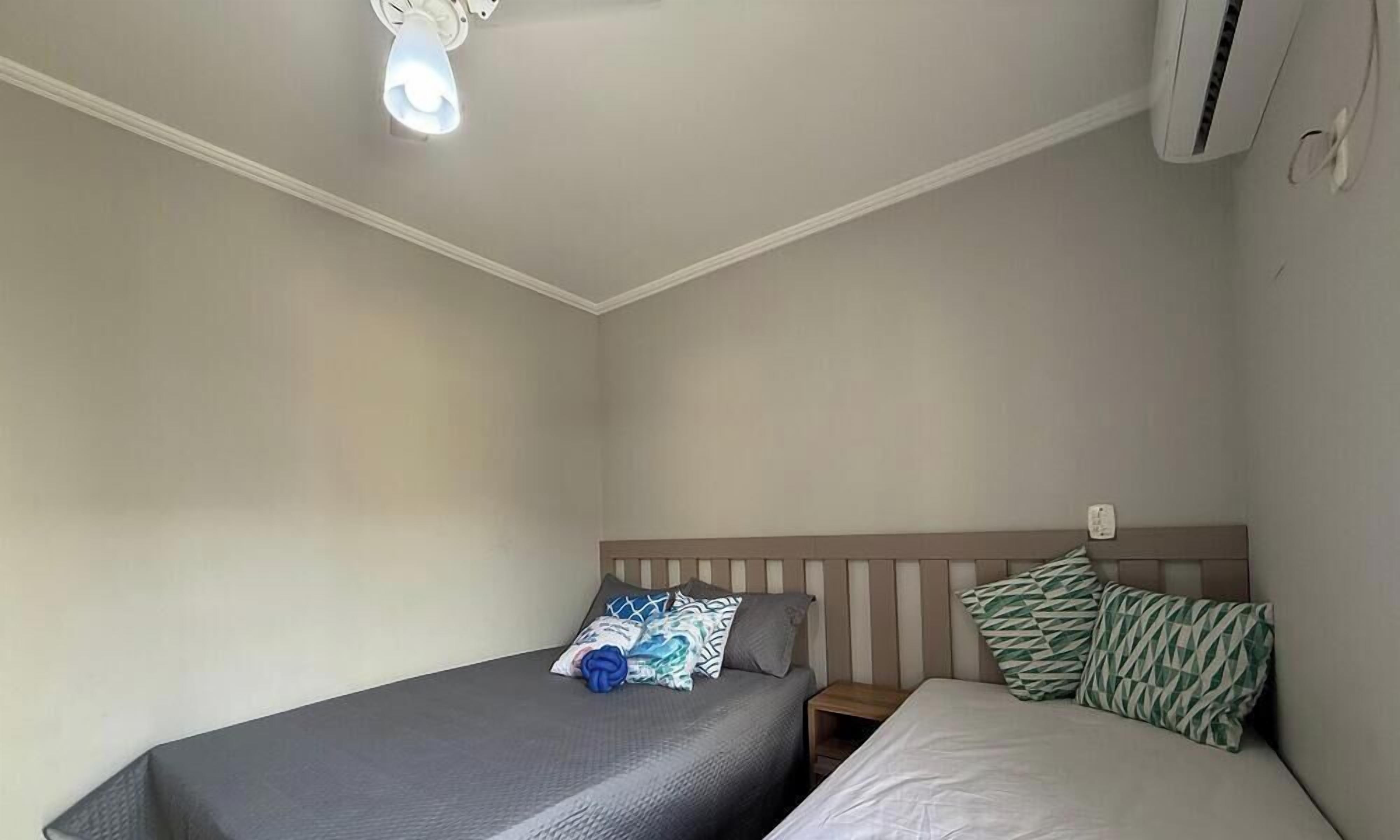 A bedroom with two beds, a nightstand, and a ceiling light.