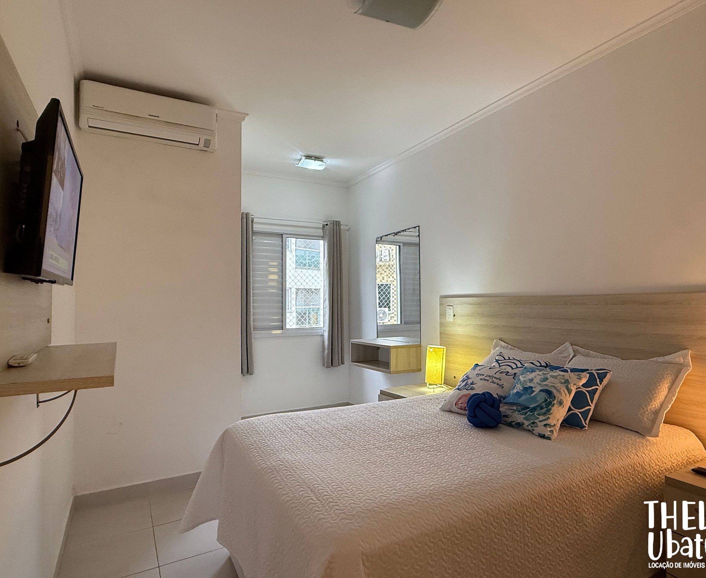 A bedroom with a bed, a TV, a window, and a mirror.