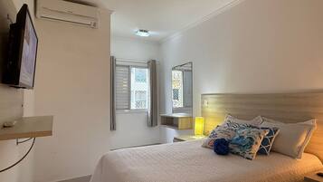 A bedroom with a bed, a TV, a window, and a mirror.