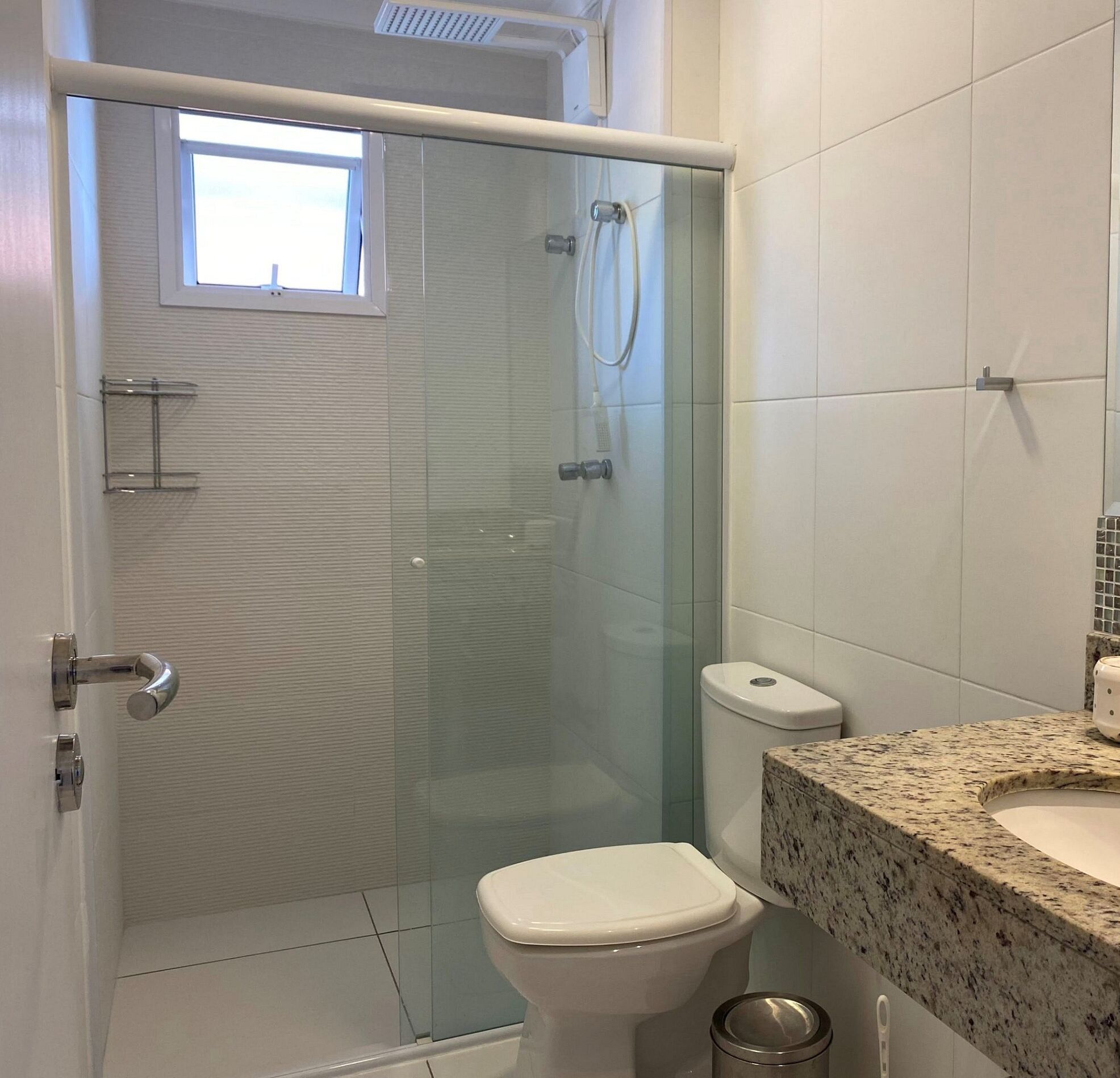 Een badkamer met een douche met glazen wand, een toilet en een wastafel met een granieten blad.