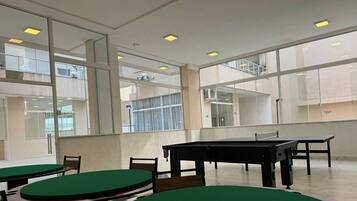 A spacious indoor area with multiple tables and chairs, large windows, and ceiling lights.