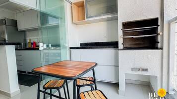 Una cocina compacta con una mesa de madera y taburetes, una puerta de cristal y una pequeña encimera con electrodomésticos.