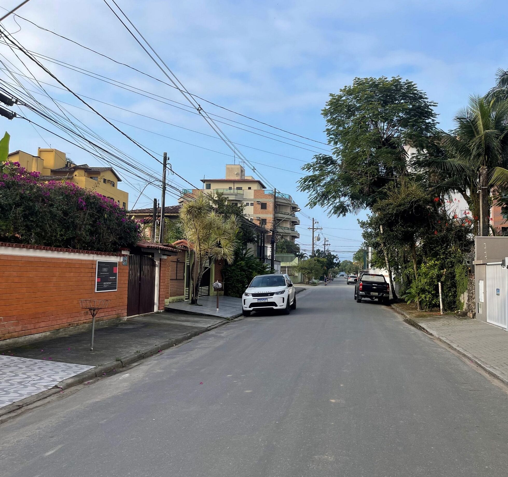 A residential street with houses, a white car parked on the side, and a black truck in the distance.