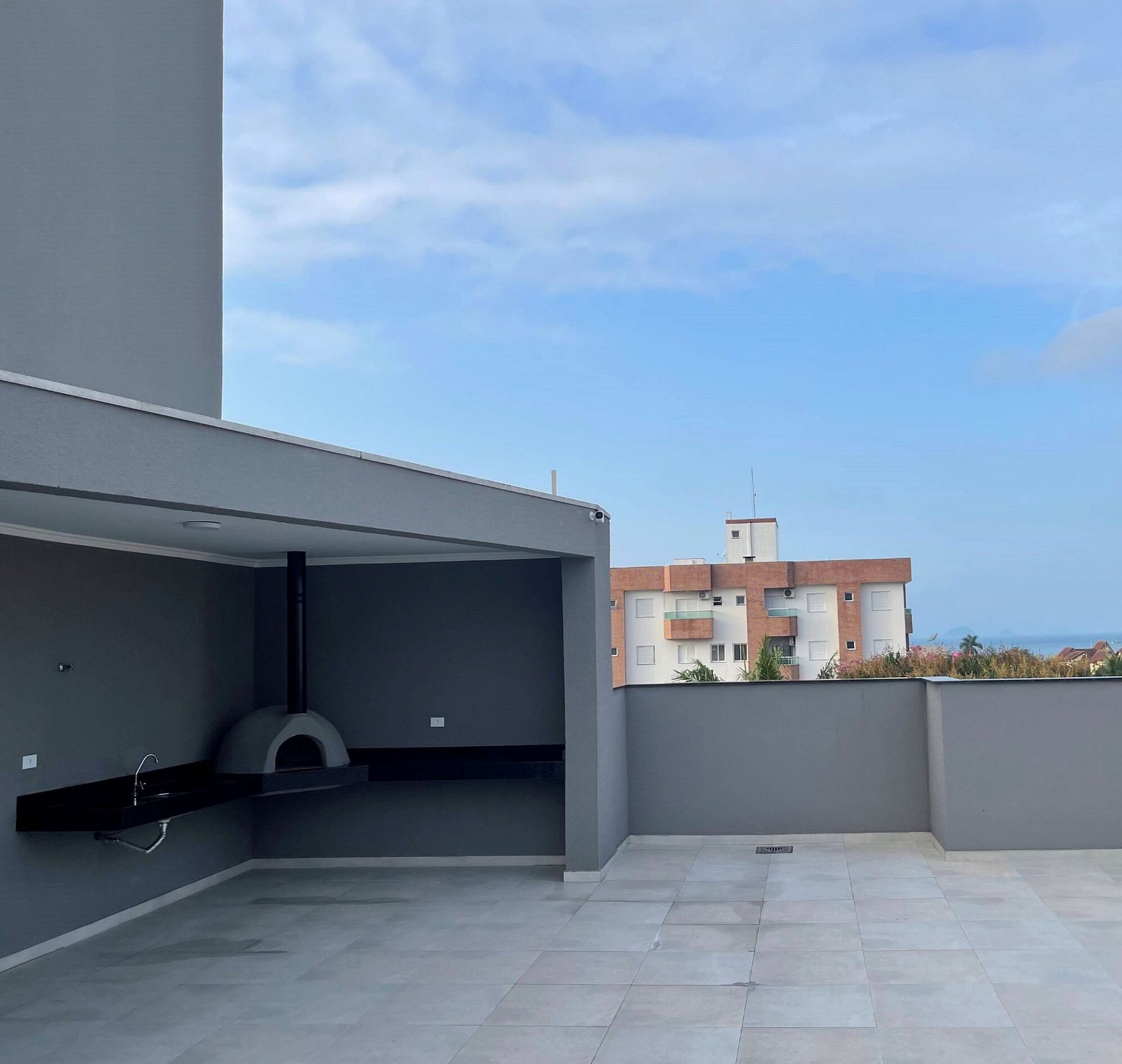 Una terraza en la azotea con diseño moderno, que cuenta con techo plano, una parrilla empotrada y vistas a un edificio residencial al fondo.