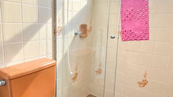 A bathroom with a toilet, a glass shower enclosure, and a window with a towel hanging on the outside.