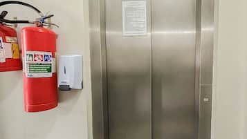 Elevador metálico com extintor de incêndio e painel de controle na parede.