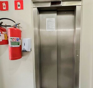 Elevador metálico com extintor de incêndio e painel de controle na parede.