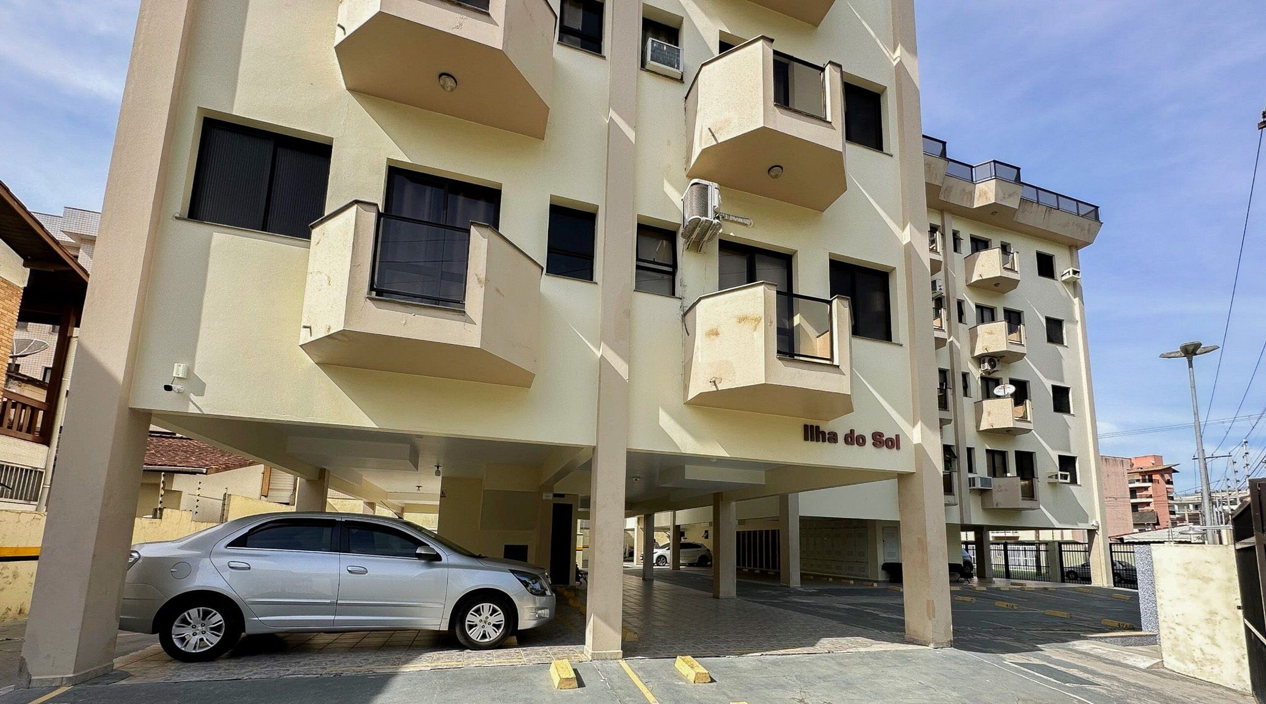 Um edifício com vários andares e varandas, um carro estacionado em frente, e o nome 