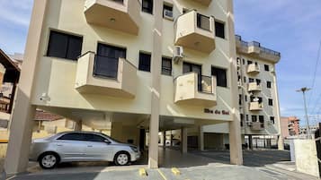 Um edifício com vários andares e varandas, um carro estacionado em frente, e o nome