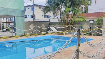 Piscina cercada por uma grade, com palmeiras e edifícios ao fundo.