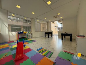 Um quarto espaçoso com área de recreação, com tapetes de espuma coloridos, um escorrega pequeno e uma casinha.