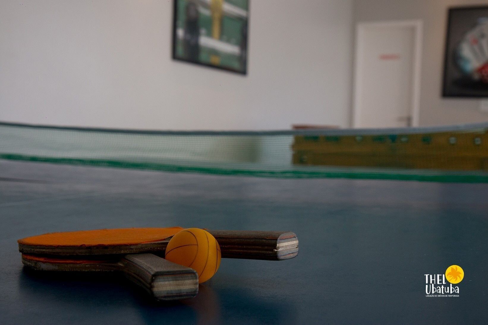 A ping pong table with a ball and paddles in a room with a white wall and a door in the background.