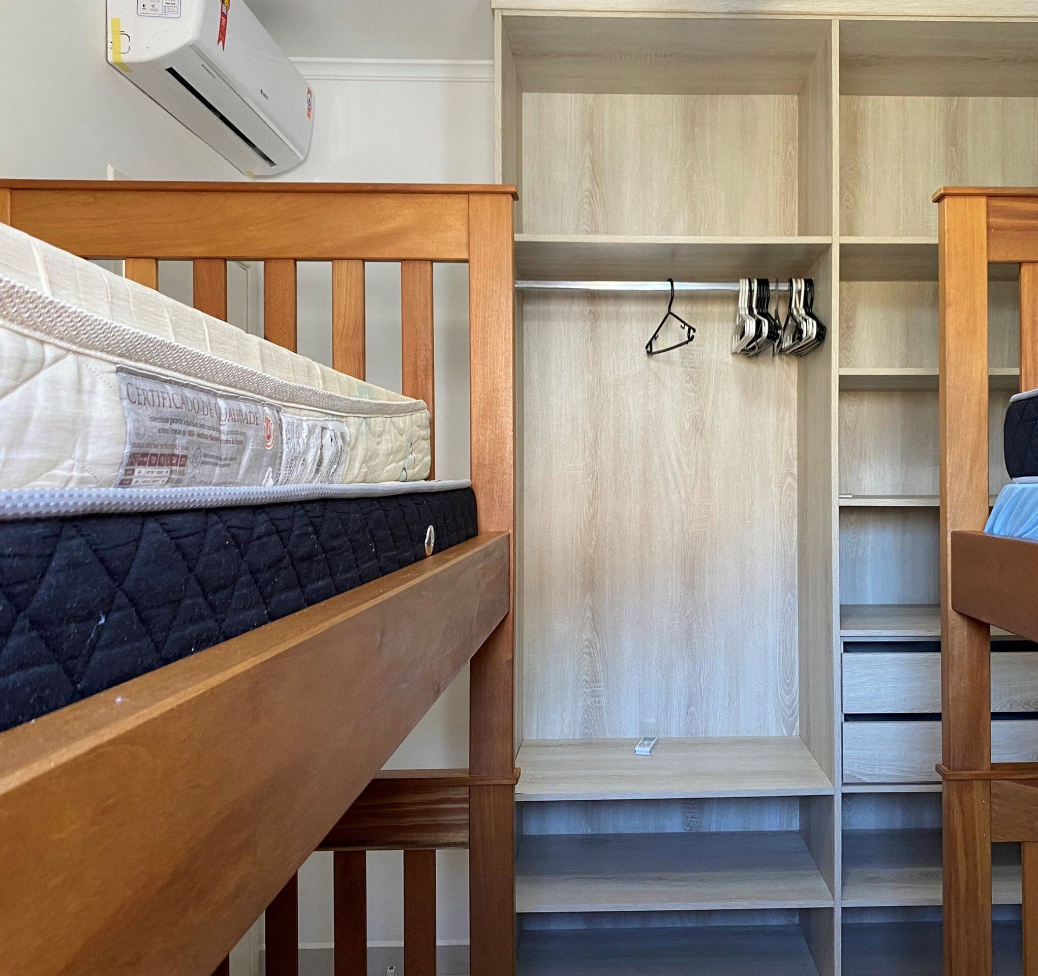Un dormitorio con cama de madera, armario con espacio para colgar y aire acondicionado integrado.