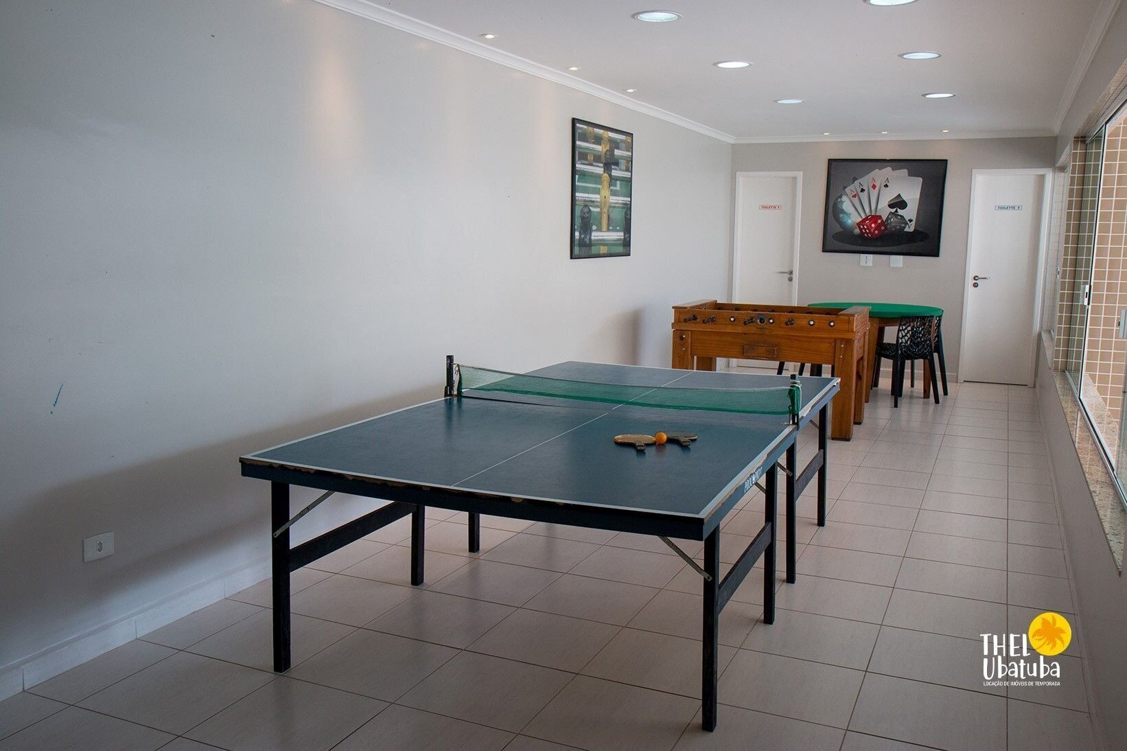 Una habitación con una mesa de ping pong, una mesa de madera con sillas y una puerta que dice 'ENTRANCE'.
