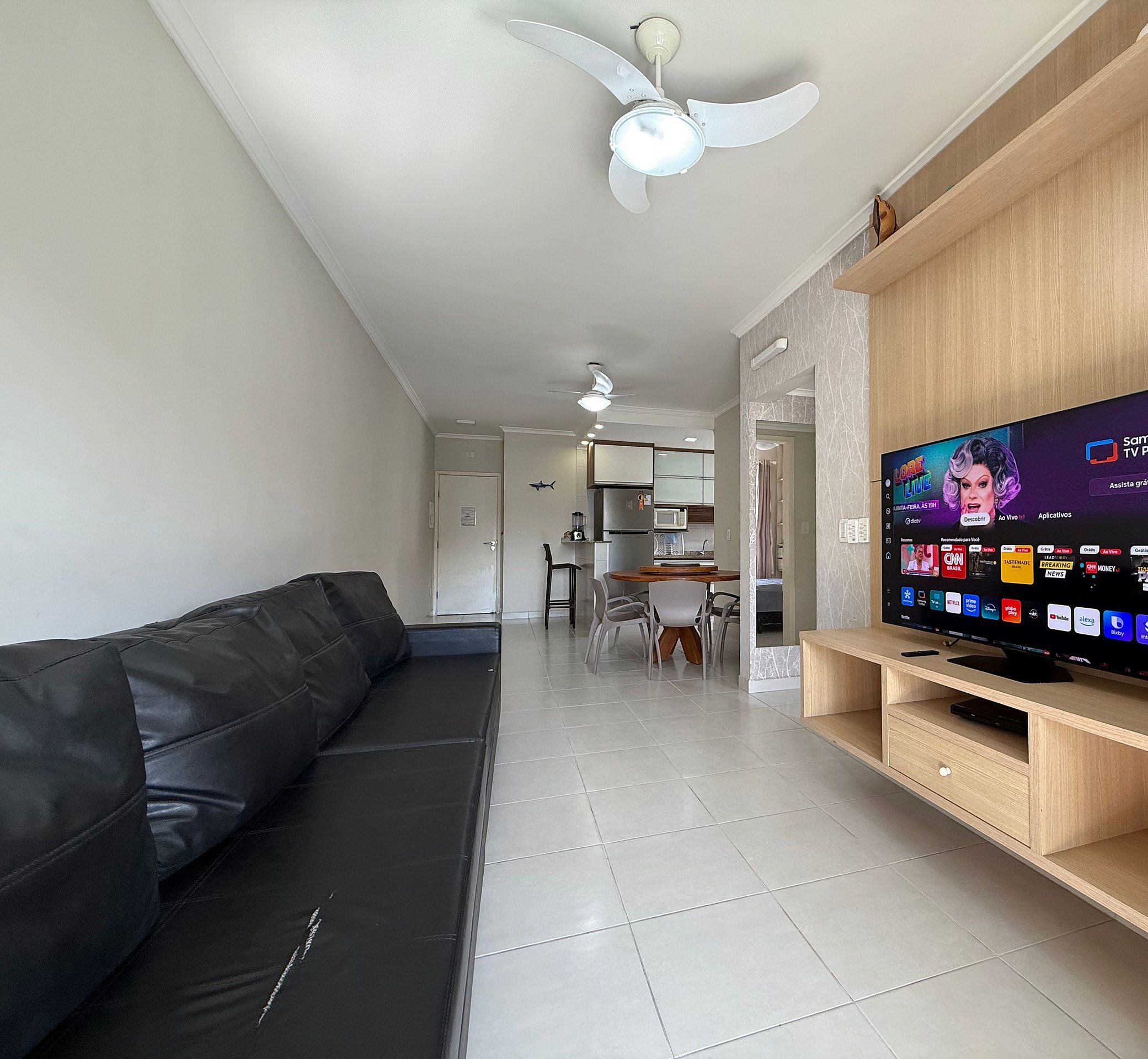 Una sala de estar moderna con un sofá de cuero negro, un mueble de televisión de madera y un ventilador de techo.