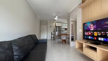 Una sala de estar moderna con un sofá de cuero negro, un mueble de televisión de madera y un ventilador de techo.