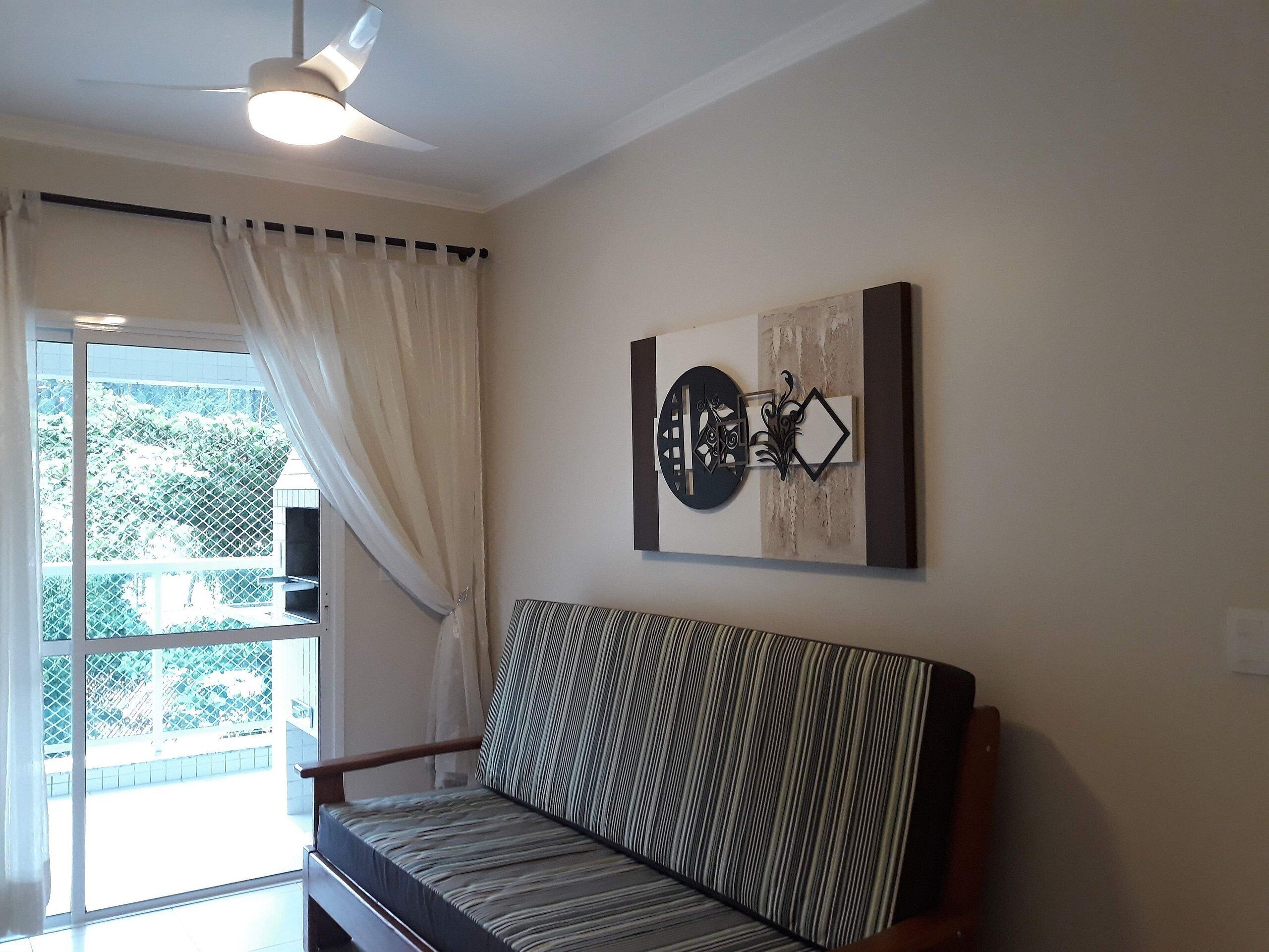 A room with a large window, a ceiling fan, a wall-mounted artwork, and a striped sofa.