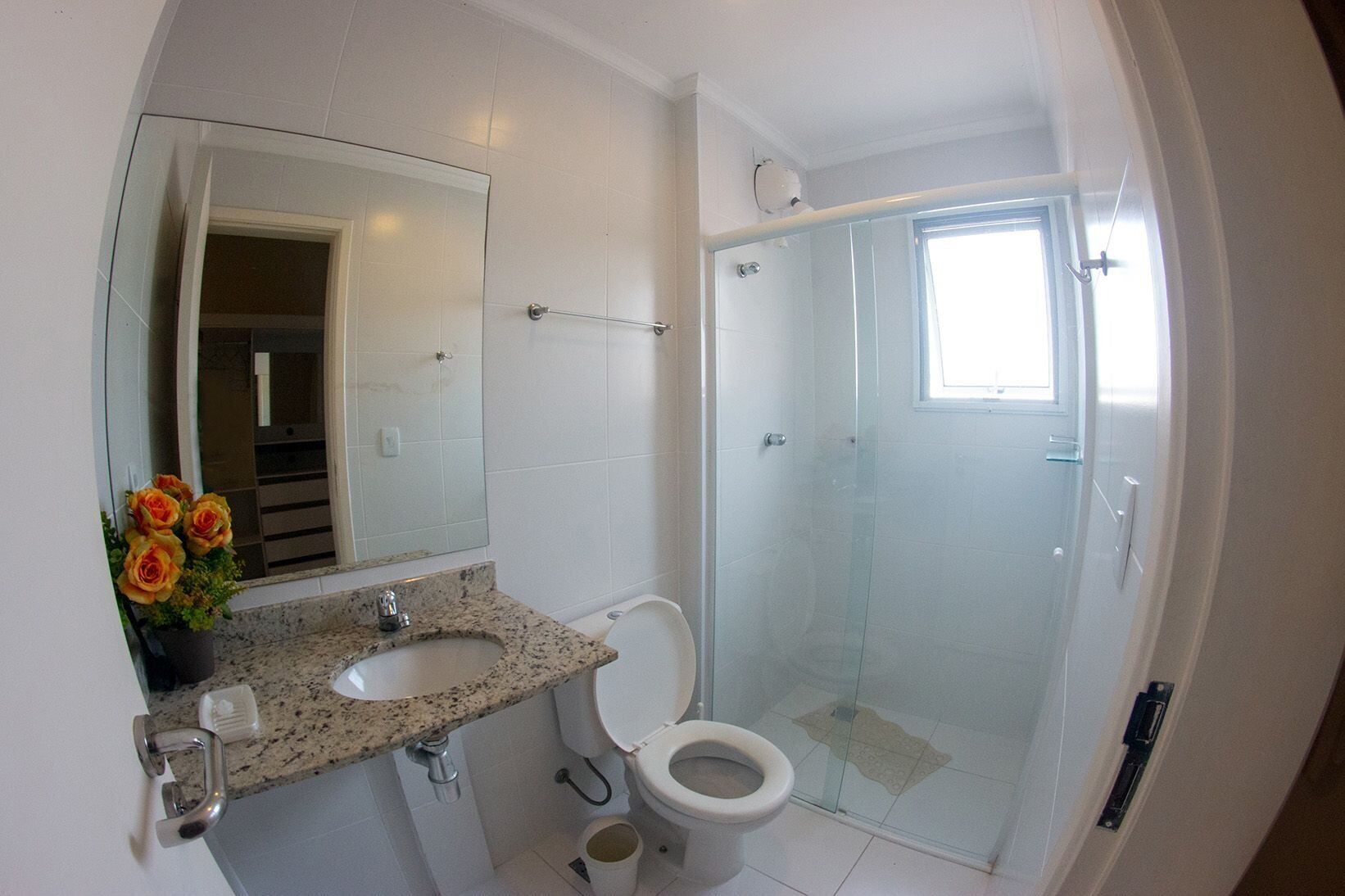 Een badkamer met een wastafel met een granieten blad, een toilet, een douche met glazen wanden en een spiegel boven de wastafel.