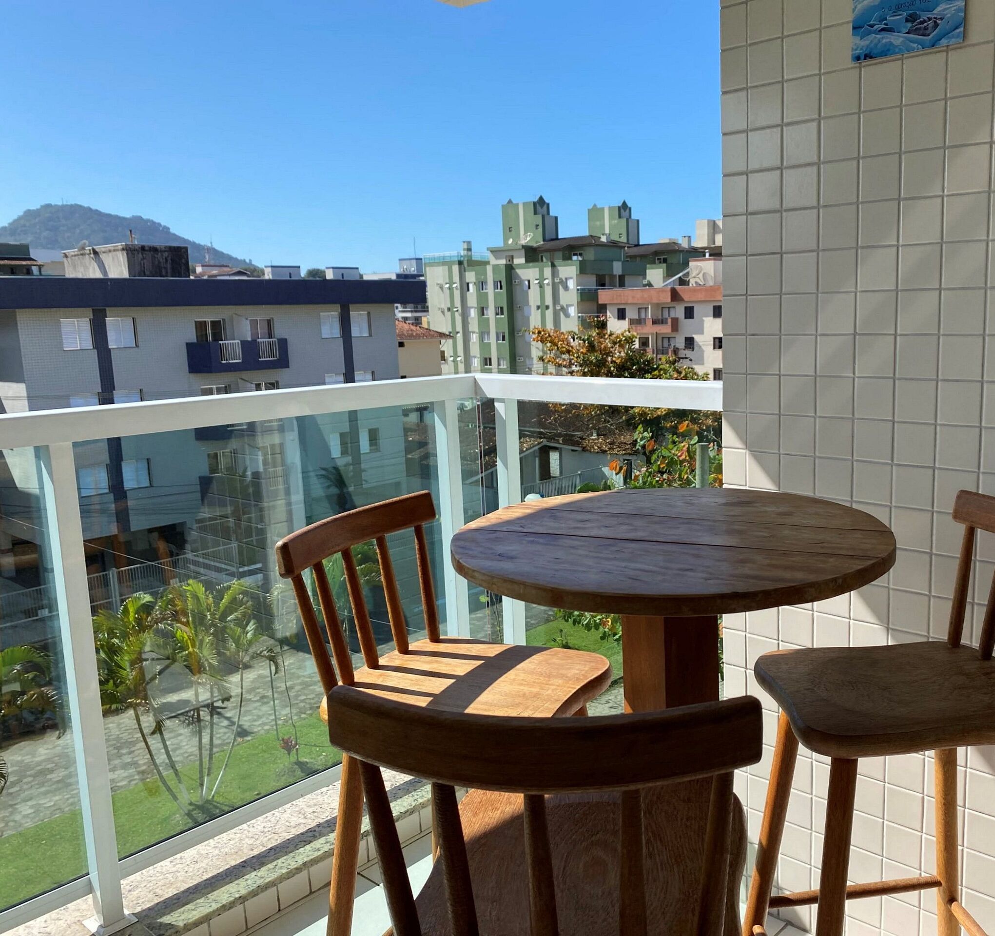 A balcony with a round wooden table and chairs, overlooking a residential area with buildings and a mountain in the distance.