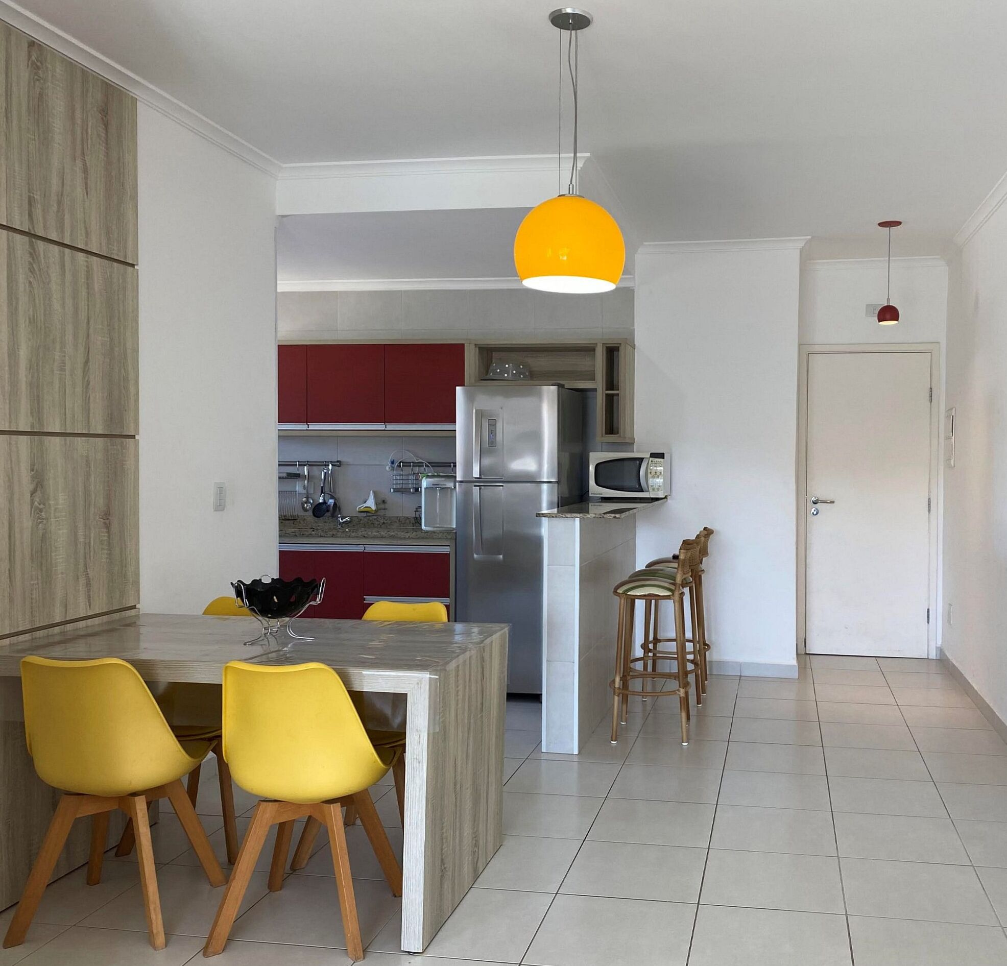 A modern kitchen with a central island, yellow chairs, a red cabinet, and a yellow pendant light.
